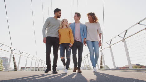 Group-Of-Young-Friends-Walking-Over-City-Bridge-Against-Flaring-Sun-Together