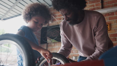 Low-angle-close-up-of-middle-aged-black-dad-helping-his-son-attach-a-wheel-to-his-racing-kart