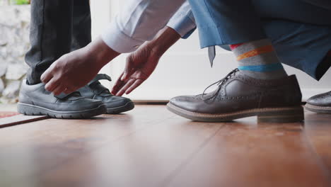 Close-up-of-father-wearing-shirt-and-tie,-brogue-shoes-and-striped-socks-kneeling-down-on-one-knee-to-fasten-the-straps-on-his-son’s-shoes-before-school,-low-section,-close-up-of-feet