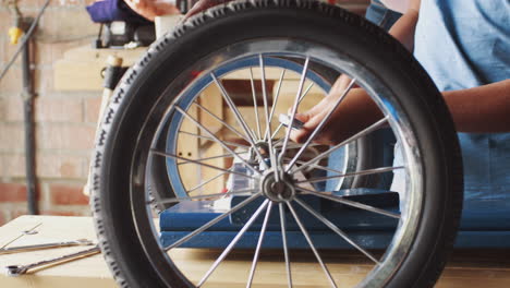 Pre-teen-boy-using-a-spanner-to-attach-a-wheel-to-his-racing-kart,-mid-section-detail,-seen-through-spokes-of-a-wheel