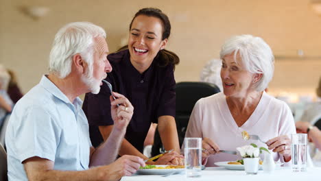 Senior-Couple-Eating-Meal-And-Talking-With-Carer-In-Retirement-Home