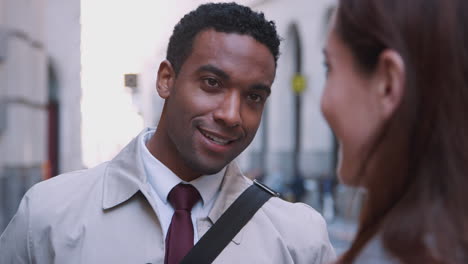 Millennial-black-businessman-standing-in-the-street-listening-his-white-female-colleague-talking,-close-up,-selective-focus