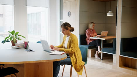 General-view-of-two-young-adult-women-working-at-computers-sitting-in-an-office,-panning-shot