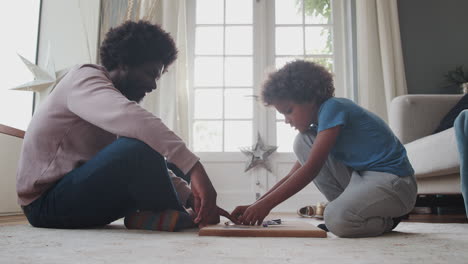 Side-view-of-a-mixed-race-pre-teen-boy-and-his-middle-aged-black-father-sitting-cross-legged-opposite-each-other-on-the-floor-playing-an-educational-game,-low-angle,-close-up