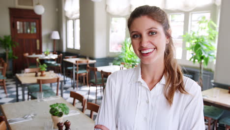 Portrait-Of-Waitress-Standing-In-Empty-Restaurant-Before-Start-Of-Service