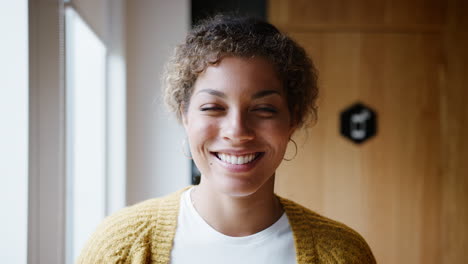 Young-mixed-race-woman-standing-by-the-window-in-an-office-laughing,-head-and-shoulders,-close-up