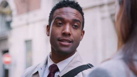 Millennial-black-businessman-standing-in-the-street-talking-with-his-white-female-colleague,-close-up,-selective-focus