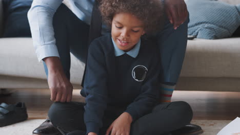 Close-up-of-mixed-race-pre-teen-boy-in-school-uniform-sitting-on-the-floor-at-home-doing-his-homework-helped-by-his-father,-sitting-behind-him-on-sofa,-tilt-shot