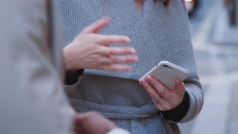 Tilt-shot-of-two-millennial-business-colleagues-holding-smartphones-and-while-talking-to-each-other,-close-up,-selective-focus