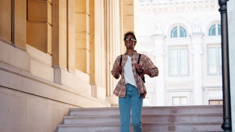 Young-black-woman-wearing-a-plaid-shirt-and-blue-jeans-walking-down-street-stairs-at-the-entrance-of-a-historical-building,-full-length