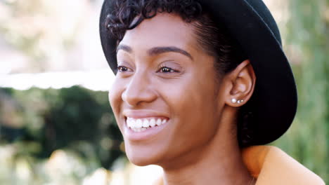 Head-shot-of-young-black-woman-with-a-curly-fringe-wearing-a-homburg-hat-laughing,-close-up
