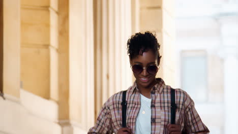 Close-up-of-a-fashionable-young-black-woman-wearing-sunglasses-and-a-plaid-shirt-walking-down-stairs-outside-a-historical-building,-selective-focus