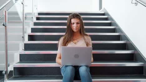 Female-High-School-Student-Sitting-On-Staircase-And-Using-Laptop