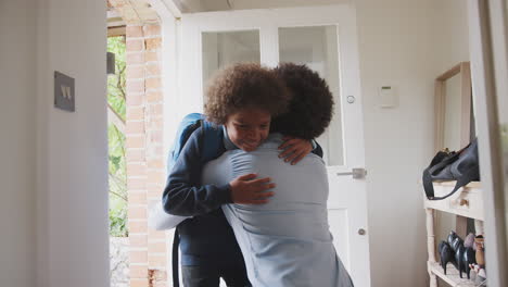 Smartly-dressed-middle-aged-black-man-man-kneeling-down-in-hallway-by-the-front-door-to-hug-and-say-goodbye-to-his-son-before-he-leaves-for-school-in-the-morning,-low-angle