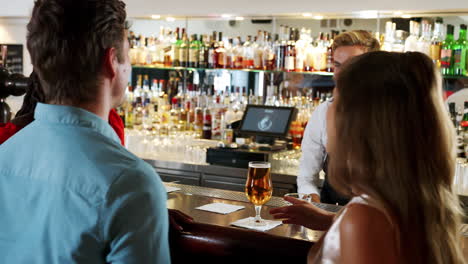 Barman-Serving-Group-Of-Young-Friends-Meeting-For-Drinks-In-Cocktail-Bar