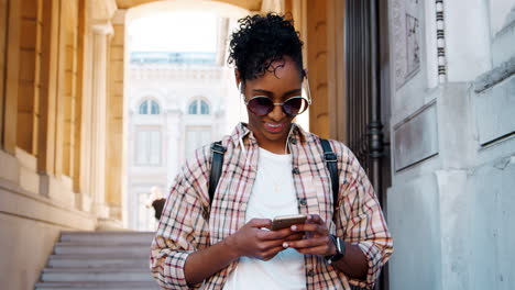 Young-adult-woman-wearing-a-plaid-shirt-standing-in-front-of-a-historical-building-entrance-using-her-smartphone