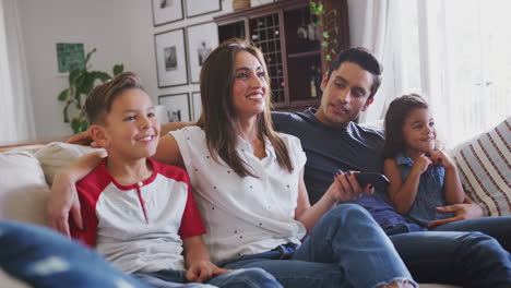 Young-Hispanic-family-sitting-on-the-sofa-at-home-watching-TV-together,-close-up