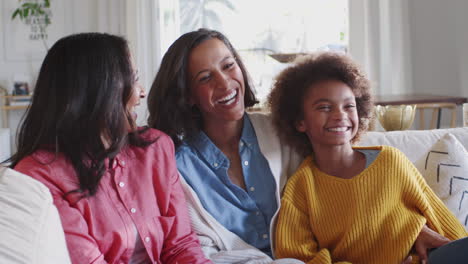 Three-generation-female-family-group-sitting-on-a-sofa-watching-TV-laughing-together,-close-up
