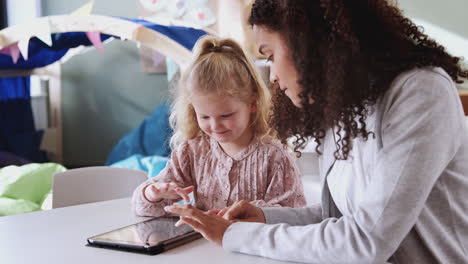 Female-infant-school-teacher-working-one-on-one-with-a-young-white-schoolgirl-using-tablet,-close-up