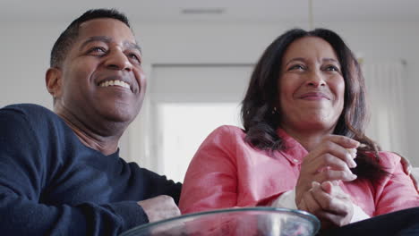 Middle-aged-African-American-couple-on-sofa-watching-TV,-laughing-and-eating-popcorn,-close-up,-low-angle