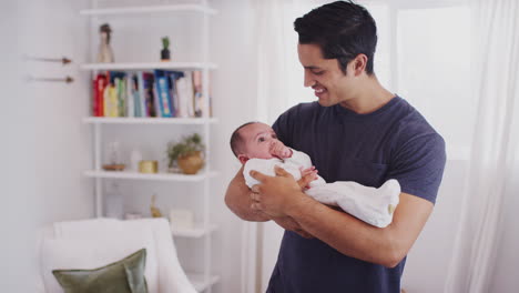 Proud-Hispanic-father-holding-his-four-month-old-child-at-home,-waist-up,-close-up