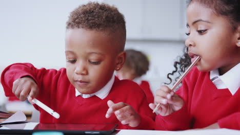 A-boy-and-girl-using-tablet-computer-and-stylus-at-a-desk-in-an-infant-school-classroom,-close-up