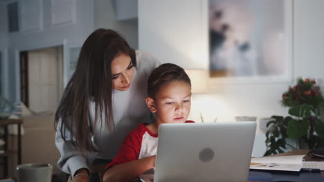Hispanic-woman-helping-her-son-while-he-does-his-homework-with-laptop-computer,-side-view,-close-up