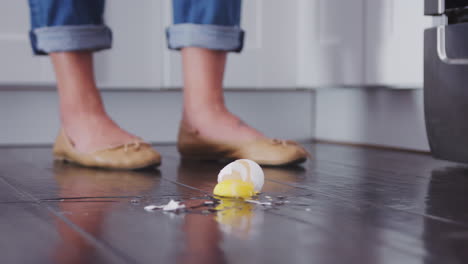 An-egg-falling-to-the-kitchen-floor-and-breaking-on-the-wooden-floorboards,-low-angle,-slow-motion