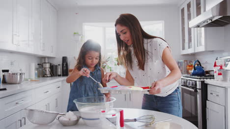 Young-girl-putting-cake-mix-into-cake-forms-while-baking-with-her-mother-in-the-kitchen,-close-up