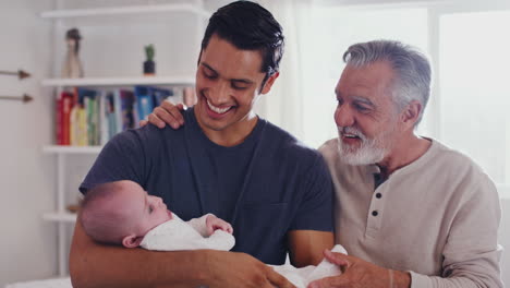 Proud-Hispanic-father-holding-his-four-month-old-son-at-home,-with-grandfather-beside-them,-close-up