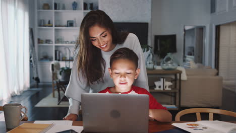 Hispanic-woman-helping-her-son-while-he-does-his-homework-with-laptop-computer,-front-view,-close-up