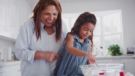 Young-girl-making-cakes-with-her-mum-and-grandmother-filling-cake-forms-with-mix,-close-up,-handheld