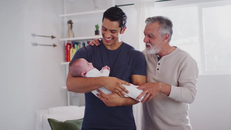 Proud-Hispanic-father-holding-his-four-month-old-son-at-home,-grandfather-standing-beside-them