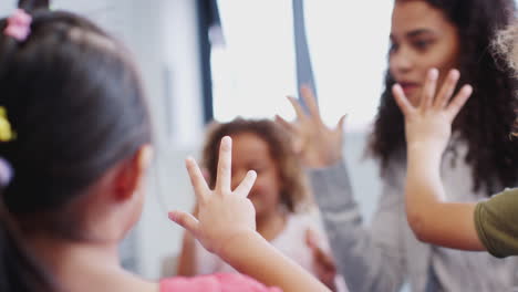 Close-up-of-infant-school-kids-and-teacher-counting-with-raised-hands-in-class,-selective-focus