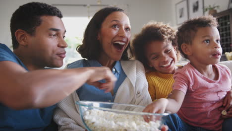 Young-African-American-family-sitting-on-the-sofa-watching-TV-and-eating-popcorn,-low-angle,-close-up