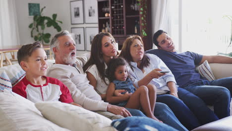 Three-generation-Hispanic-family-sitting-on-the-sofa-watching-TV,-grandmother-using-remote-control