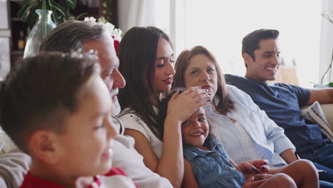 Three-generation-Hispanic-family-sitting-on-the-sofa-watching-TV-together,-close-up