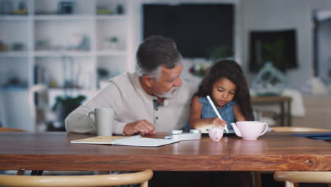 Senior-Hispanic-man-sitting-with-his-granddaughter,-who-uses-stylus-and-tablet-computer,-rack-focus