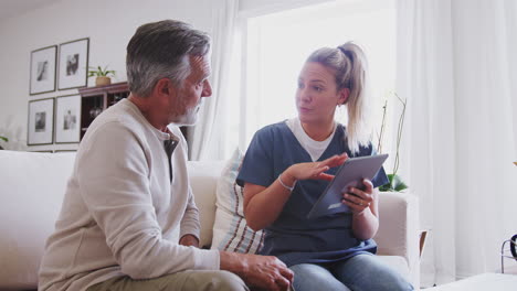 Female-healthcare-worker-using-tablet-computer-sitting-with-senior-Hispanic-man-during-a-home-visit,concern