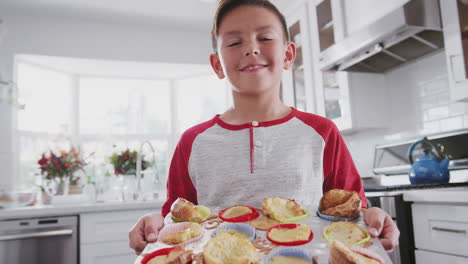 Proud-pre-teen-Hispanic-boy-standing-in-kitchen-presenting-the-cakes-he’s-made-to-camera,-close-up