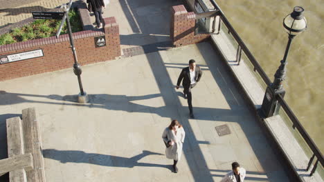 Elevated-view-of-three-city-workers-walking-on-a-sunny-urban-street-by-the-River-Thames-in-the-City-of-London,-lockdown