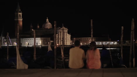 A-couple-sitting-on-the-embankment-in-front-of-the-night-Venice-view