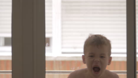 Funny-kid-fooling-with-towel-and-having-fun-view-through-the-glass