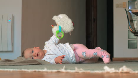 A-baby-girl-in-pink-tights-lying-on-a-floor-with-toy-sheep