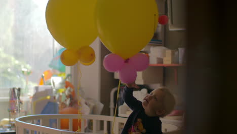A-baby-girl-standing-in-a-crib-and-playing-with-balloons