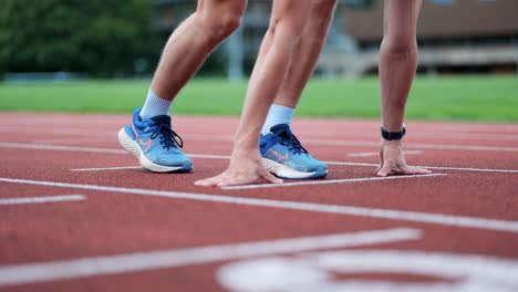 Male-runner-takes-up-starting-position-at-marker-on-running-track,-close-up-on-the-athlete's-hands-and-feet