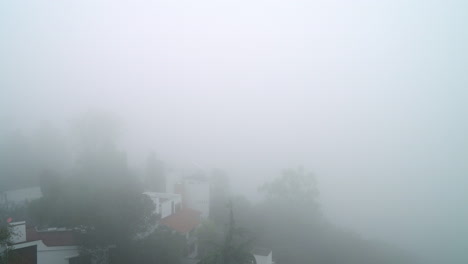 Panoramaaufnahme-Mit-Häusern,-Die-Von-Dichtem-Nebel-Umhüllt-Sind,-In-Einer-Ruhigen-Waldumgebung