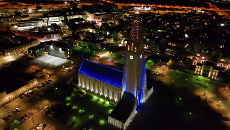 Drone-shot-circling-the-night-lit-Hallgrímskirkja-church,-in-Reykjavik,-Iceland