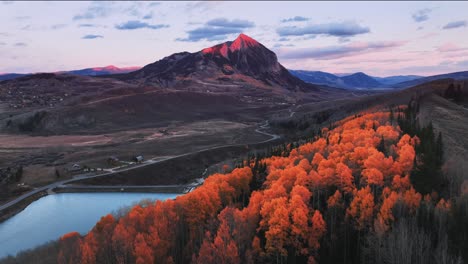 a-drone-view-of-water,-golden-and-orange-aspens,-and-the-tip-of-a-mountain-in-Crested-Butte,-CO-being-lit-up-by-alpen-glow