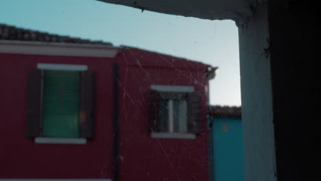 A-closeup-of-a-spiderweb-on-a-stone-opening-in-front-of-a-blurred-Burano-facade